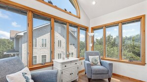 A spacious room with large windows, a white dresser, two grey armchairs, and a lamp. - 6BR Duck Resort | Hot Tub, Beach & Village Walk (Duck)