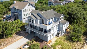 A large, multi-story house with a balcony, surrounded by trees and other houses. - 6BR Duck Resort | Hot Tub, Beach & Village Walk (Duck)