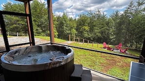 Un jacuzzi en un balcón con vistas a un bosque y dos sillones Adirondack rojos.