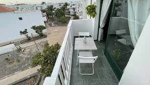 A balcony with a white table and chairs, a hanging plant, and a view of a residential area. - Mamarosa Fuerteventura: Family Base 5 min from the Airport + Telework Space (Nuevo Horizonte)
