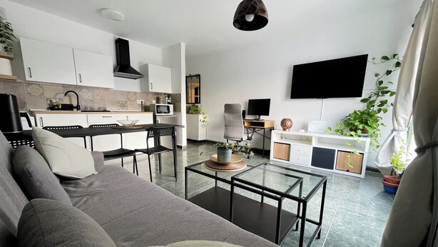 A modern living room with a sofa, coffee table, and TV. There is a kitchen area with cabinets and a microwave. - Mamarosa Fuerteventura: Family Base 5 min from the Airport + Telework Space (Nuevo Horizonte)