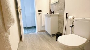 A modern bathroom with a toilet, sink, and mirror. A towel hangs on the wall, and a door leads to another room. - Mamarosa Fuerteventura: Family Base 5 min from the Airport + Telework Space (Nuevo Horizonte)