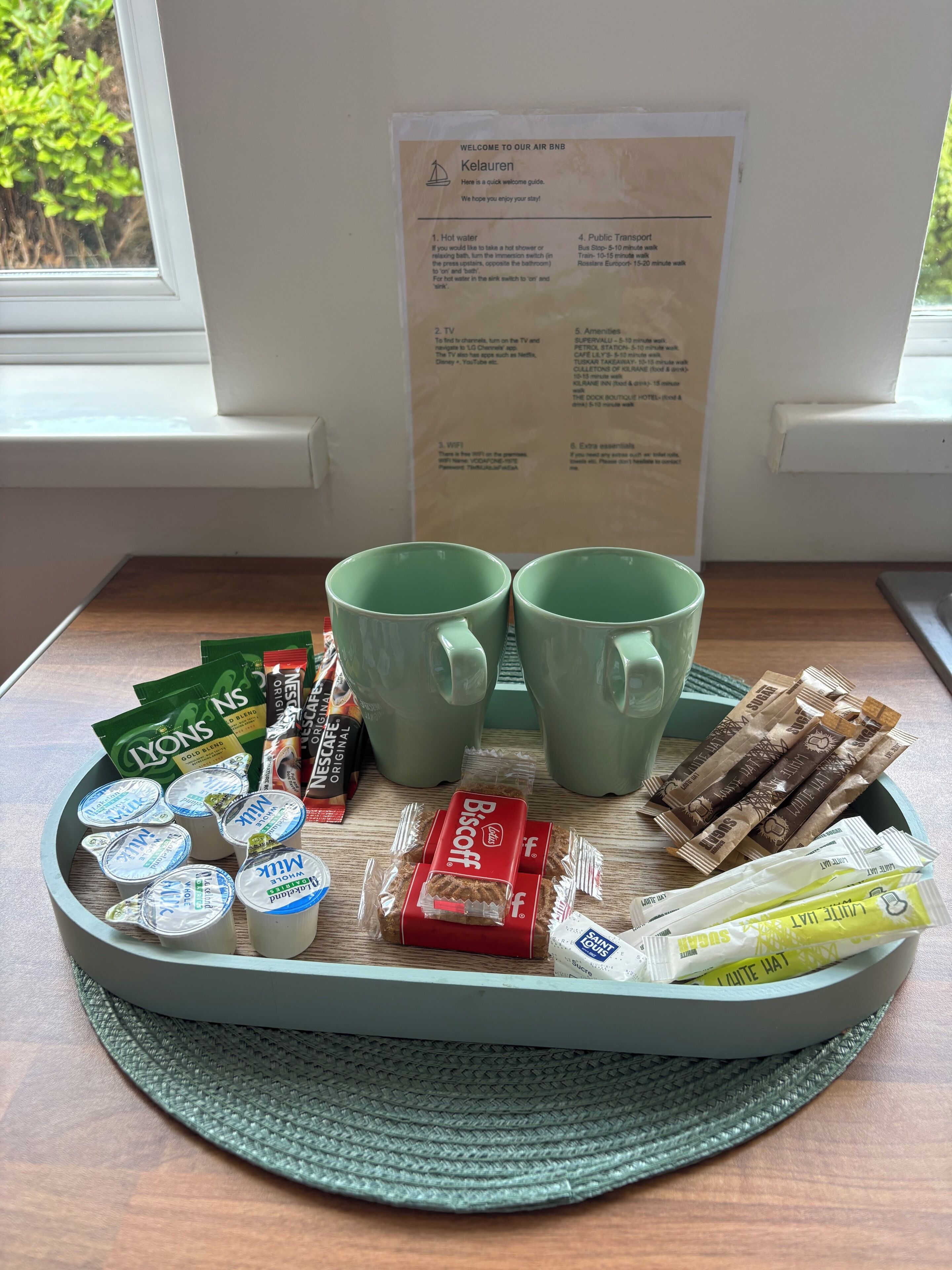 Ein Tablett mit Frühstücksartikeln, darunter Milch, Joghurt, Kekse und Kaffeepäckchen, auf einer gewebten Unterlage.