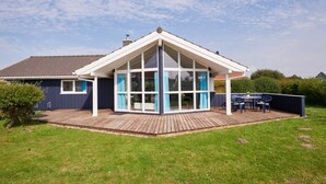 A house with a large glass conservatory, a wooden deck, and a fenced backyard. - 4 Star Holiday Home in Friedrichkoog (Friedrichskoog)