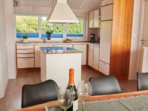 A kitchen with a dining area, wooden cabinets, a window with a view, and a bottle of wine on the table. - 4 Star Holiday Home in Friedrichkoog (Friedrichskoog)