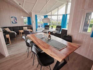 A dining area with a wooden table, black chairs, and a view of the outdoors through large windows. - 4 Star Holiday Home in Friedrichskoog (Friedrichskoog)