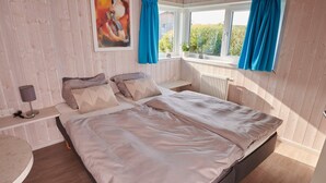 A bedroom with a bed, a bedside table with a lamp, a window with curtains, and a painting on the wall. - 4 Star Holiday Home in Friedrichkoog (Friedrichskoog)