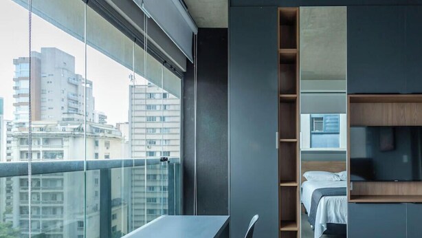 Een moderne hotelkamer met balkon, bed, televisie en bureau met stoelen.