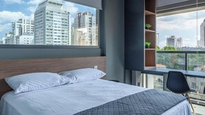 Een moderne hotelkamer met een groot bed, een inbouwkastje met planten en uitzicht op de stad.