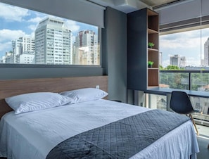 A modern hotel room with a large bed, a built-in shelf with plants, and a city view.