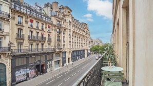 Straßenansicht mit einer Reihe von Gebäuden, blauem Himmel und einem Balkon mit Tisch und Stühlen.