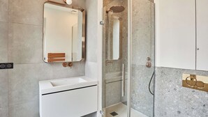 Ein modernes Badezimmer mit einem weißen Waschbecken, einem großen Spiegel und einer Duschkabine aus Glas.