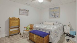 Un dormitorio con cama, un cofre de madera, una silla, una mesita de noche y un ventilador de techo.