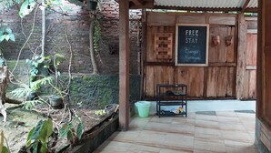 A rustic wooden structure with a tiled floor, a metal shelf with shoes, and a chalkboard sign offering free Wi-Fi. - Banyu Kasongan Homestay (Bangunjiwo)