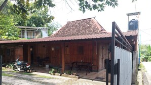 A wooden house with a tiled roof, a motorcycle parked outside, and a gated entrance. - Banyu Kasongan Homestay (Bangunjiwo)