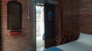 A room with a brick wall, a wooden door, a bed with white bedding, and a blue mat. - Banyu Kasongan Homestay (Bangunjiwo)