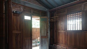 A room with wooden walls and a bed with a blue cover. There is a window with bars and a door leading outside. - Banyu Kasongan Homestay (Bangunjiwo)