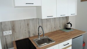 A kitchen with white cabinets, a stainless steel sink, a wooden countertop, and a kettle. - Apartment in Mrzezyno by Sandy Beaches (Trzebiatow)