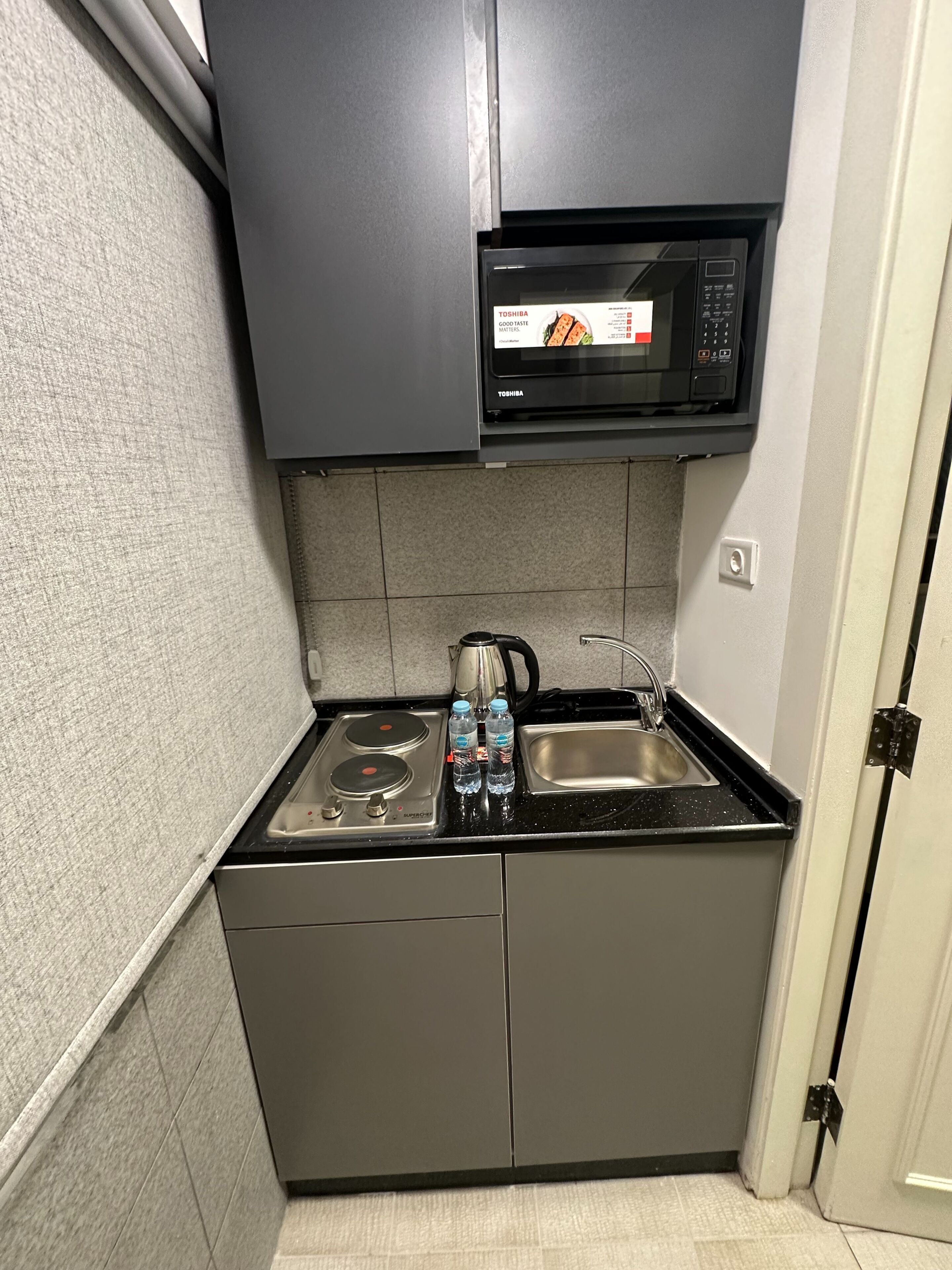 Una cocina compacta con microondas integrado, estufa a gas y lavamanos.