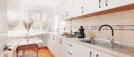 Una cocina moderna con armarios blancos, estufa a gas, un lavamanos y una ventana con vistas a árboles.