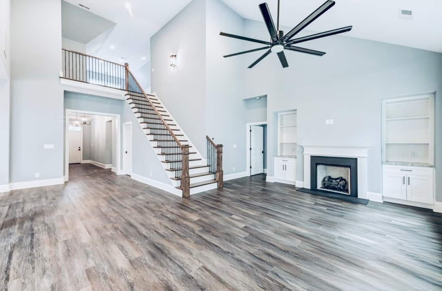 Ein geräumiges Wohnzimmer mit einer Holztreppe, einem Kamin und einem Deckenventilator.