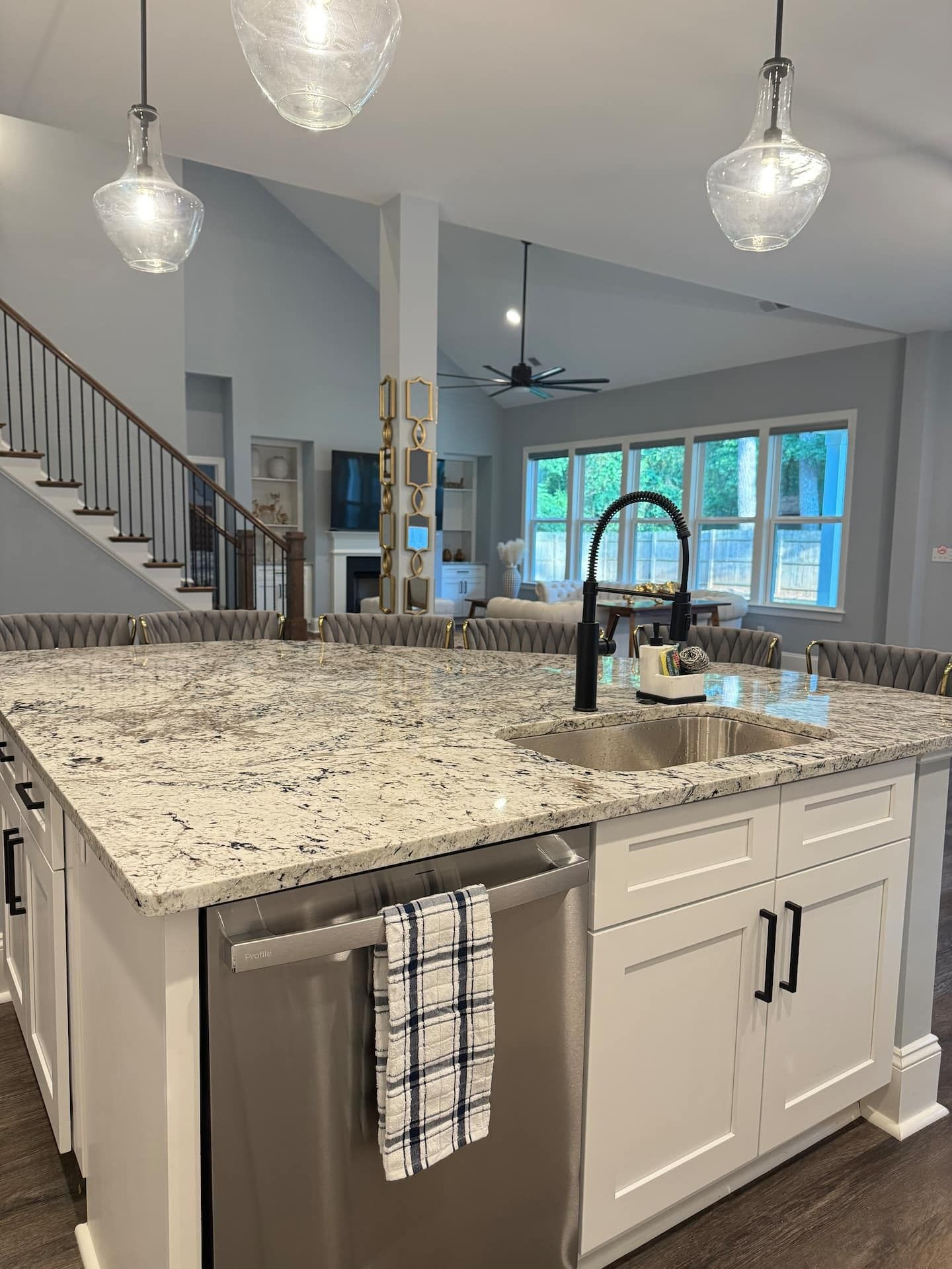 A kitchen with a large island, white cabinetry, a stainless steel dishwasher, and pendant lighting.