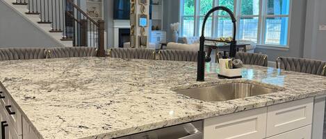 A kitchen with a large island, white cabinetry, a stainless steel dishwasher, and pendant lighting.