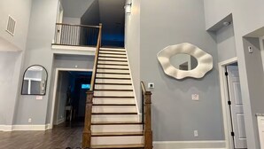 A spacious interior with a wooden staircase leading to a mezzanine, a large mirror on the wall, and a door on the right. - Beautiful Escape, Mins from Carowinds & Lake Wylie (Charlotte)