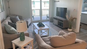 Ein Wohnzimmer mit Sofa, Couchtisch, Fernseher und einem Balkon.