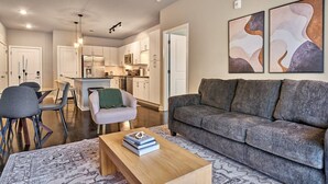Ein modernes Wohnzimmer mit grauem Sofa, einem Holztisch mit Büchern, einem gemusterten Teppich und einem Essbereich mit Stühlen und Tisch.