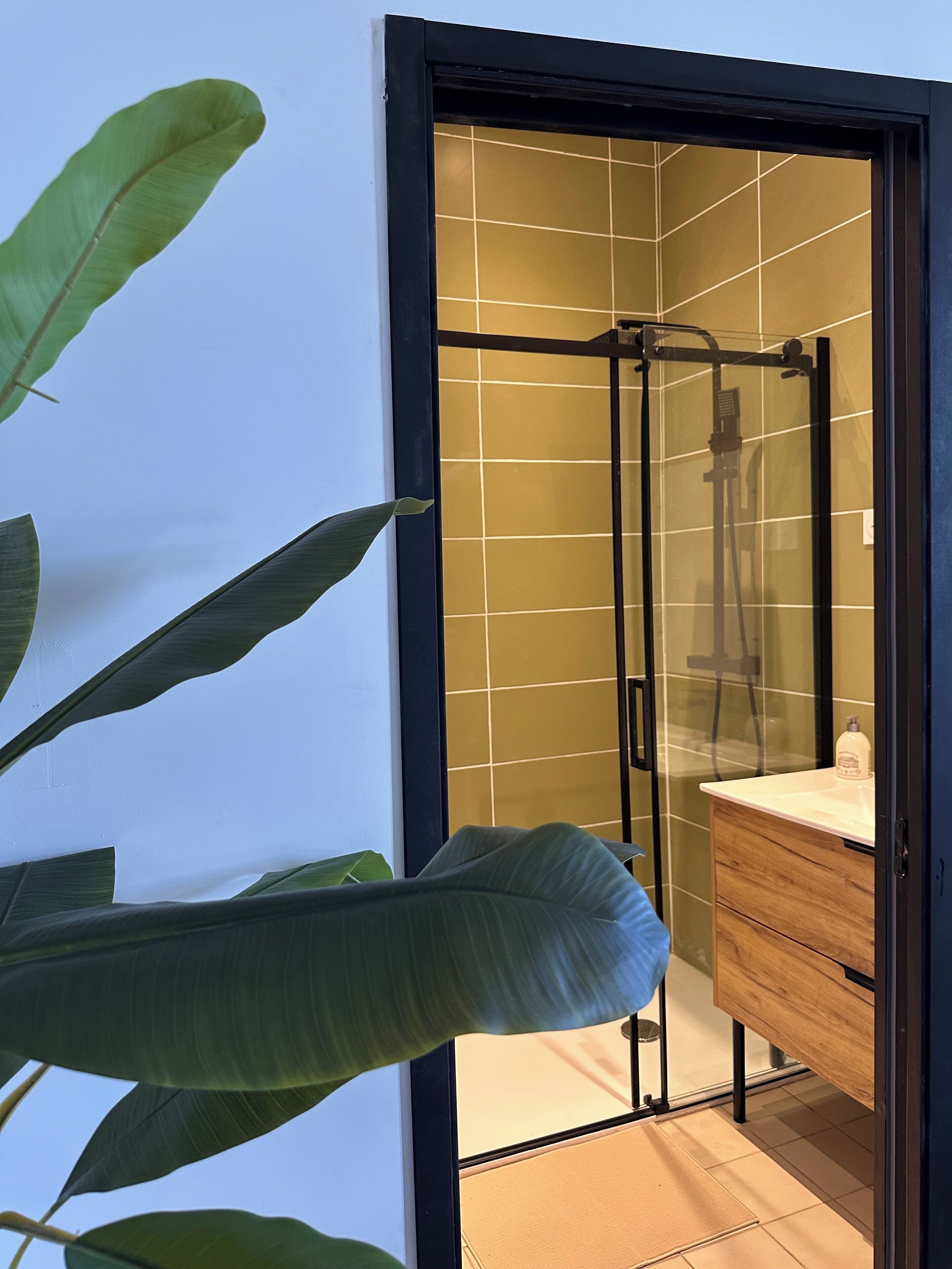 Un baño moderno con cabina de ducha de vidrio, tocador de madera y una planta grande.