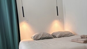 A neatly made bed with a wooden frame and a light-colored duvet, two bedside lamps, and a teal curtain. - Design & Comfort apartment ! Sleeps 4 (Périgueux)
