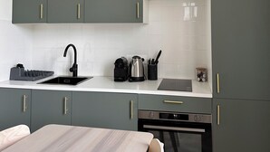 A modern kitchen with dark green cabinets, a white countertop, a black faucet, a coffee maker, a kettle, and a built-in oven. - Design & Comfort apartment ! Sleeps 4 (Périgueux)