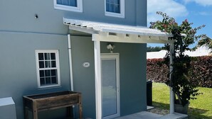 A two-story house with a covered porch, a wooden bench, and a small garden area. - Charming 1-bedroom apartment centrally located to all that Bermuda has to offer (Devonshire)