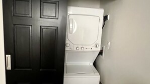 A compact laundry room with a washer and dryer, a dark door, and a white wall. - Charming 1-bedroom apartment centrally located to all that Bermuda has to offer (Devonshire)