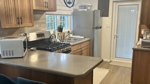 A modern kitchen with wooden cabinets, a central island with bar stools, stainless steel appliances, and a pendant light. - Charming 1-bedroom apartment centrally located to all that Bermuda has to offer (Devonshire)