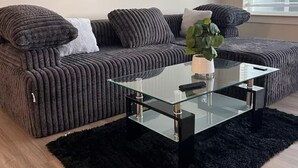 A modern living room with a sectional sofa, a glass coffee table, and a black rug.