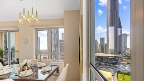Un coin repas avec une table dressée pour quatre personnes, de grandes fenêtres et une vue sur le paysage urbain, avec ses nombreux immeubles de grande hauteur.