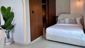 Une chambre à coucher avec un lit, une armoire en bois, une plante en pot et un luminaire.