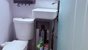 Une salle de bain équipée de toilettes, d’un lavabo et d’un petit marchepied sur lequel sont posés les articles de toilette.