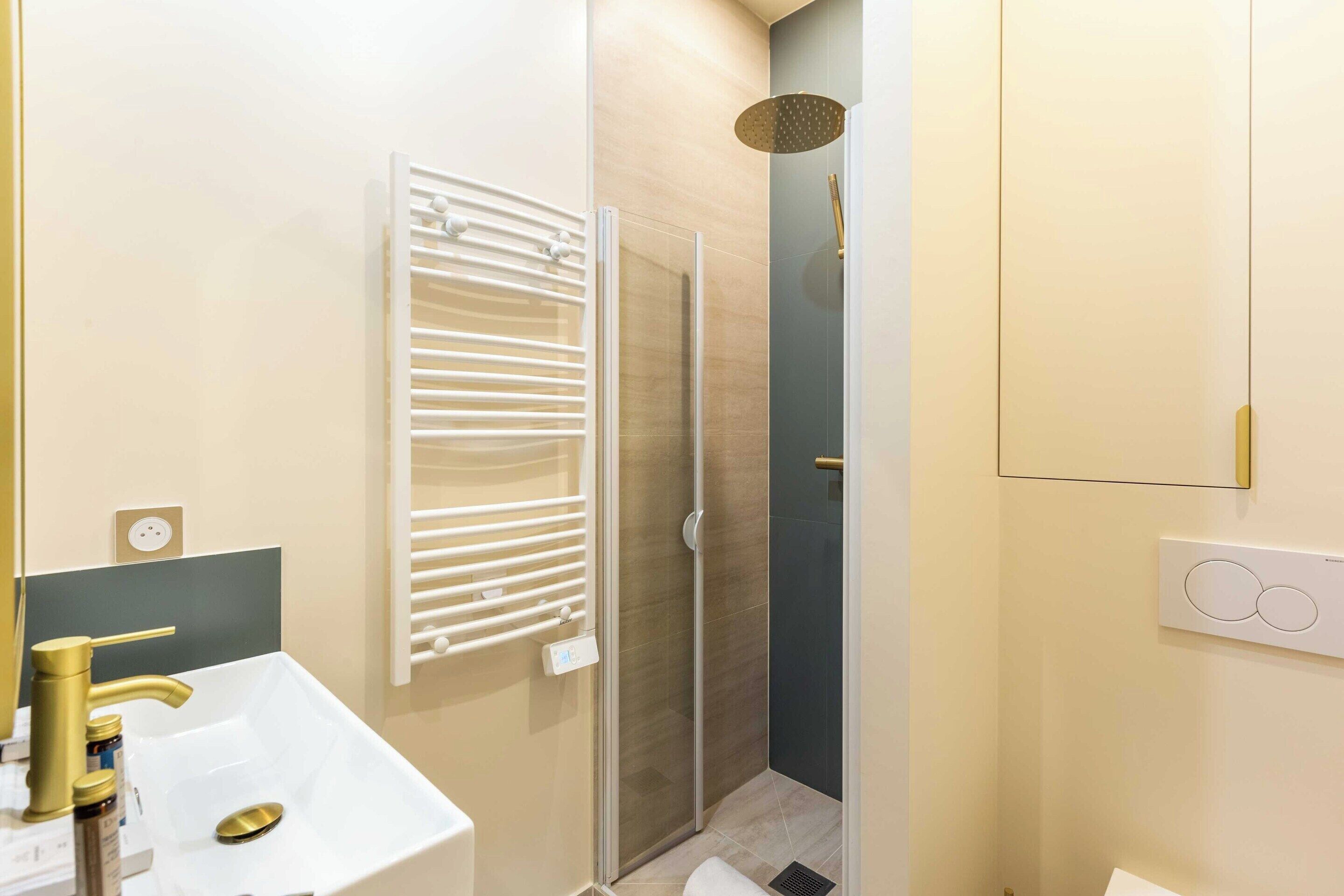 Un baño moderno con lavamanos blanco, grifo dorado y cabina de ducha con paredes de vidrio.