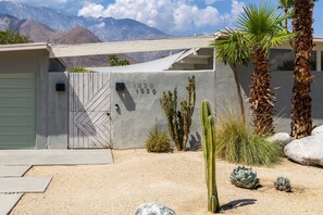 A desert-style house with a garage, cacti, and palm trees.