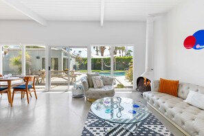 A modern living room with a glass coffee table, a sofa, and a dining area with chairs.