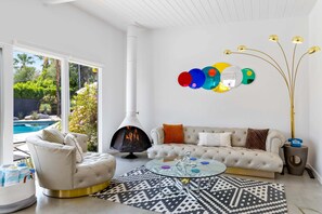 A modern living room with a fireplace, a sofa, a coffee table, and a view of a pool.