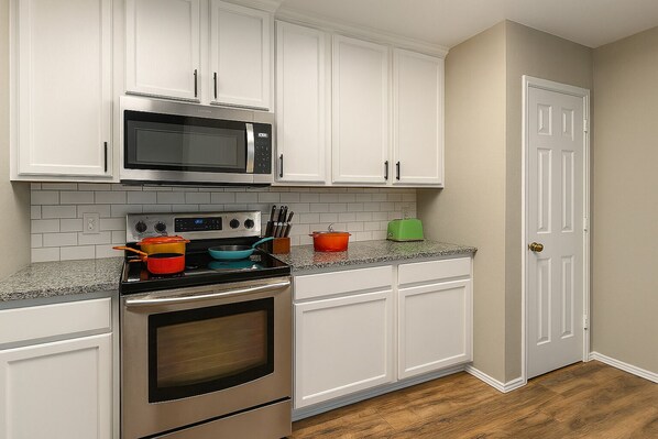 A kitchen with white cabinets, a microwave, an oven, and a granite countertop. - Crew Stay Sleeps 16 Work Cook Play Relax (Aubrey)