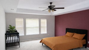 Een slaapkamer met een bed, een plafondventilator, een raam met jaloezieën en een plant.