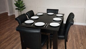 Een eettafel gedekt voor zes personen, met zwarte stoelen, witte borden en bestek.