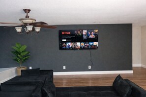A living room with a flat-screen TV mounted on the wall displaying a Netflix interface. - Crew Stay Sleeps 16 Work Cook Play Relax (Aubrey)