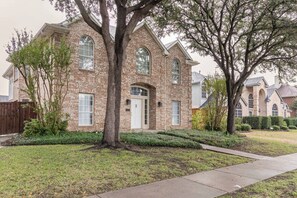 A two-story brick house with a central entrance, a large tree in front, and a well-maintained lawn. - Spacious Home Quiet Neighborhood nr Downtown (Carrollton)