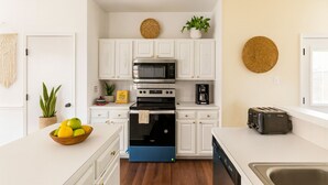 A compact kitchen with white cabinets, a black oven, a coffee maker, and a toaster. There is a plant on the counter and a basket of lemons. - Spacious Home Quiet Neighborhood nr Downtown (Carrollton)